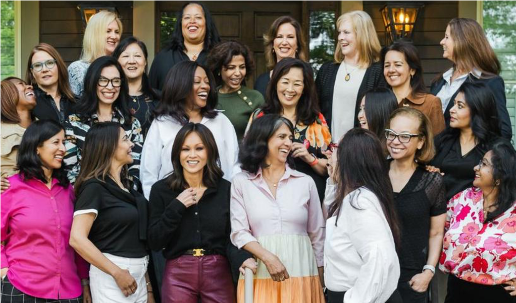 Women smiling and talking together at an outdoor gathering.